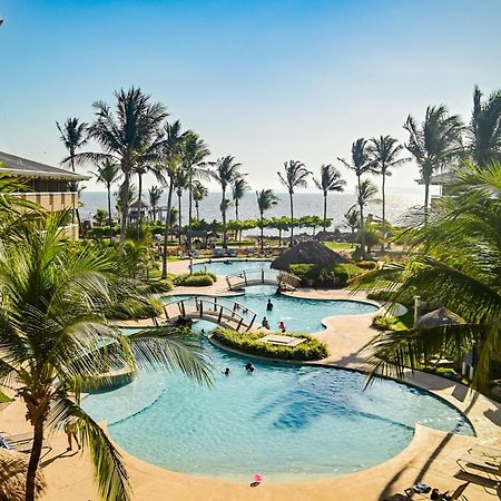 Fiesta Resort All Inclusive Central Pacific - Costa Rica El Roble Exterior photo The photo depicts a vibrant tropical scene featuring a large swimming pool surrounded by palm trees. The pool area has a curved shape and is situated in a sunny environment, suggesting a warm climate. There are several people enjoying the water, and 