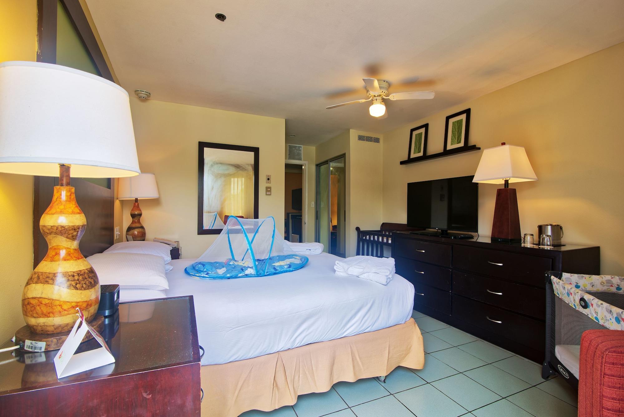 Fiesta Resort All Inclusive Central Pacific - Costa Rica El Roble Exterior photo The photo shows the interior of a hotel room. There is a large bed with white bedding, complemented by a light-colored bed skirt. Next to the bed, there's a wooden bedside table with a lamp and a small triangular decorative item. A mirror hangs on th