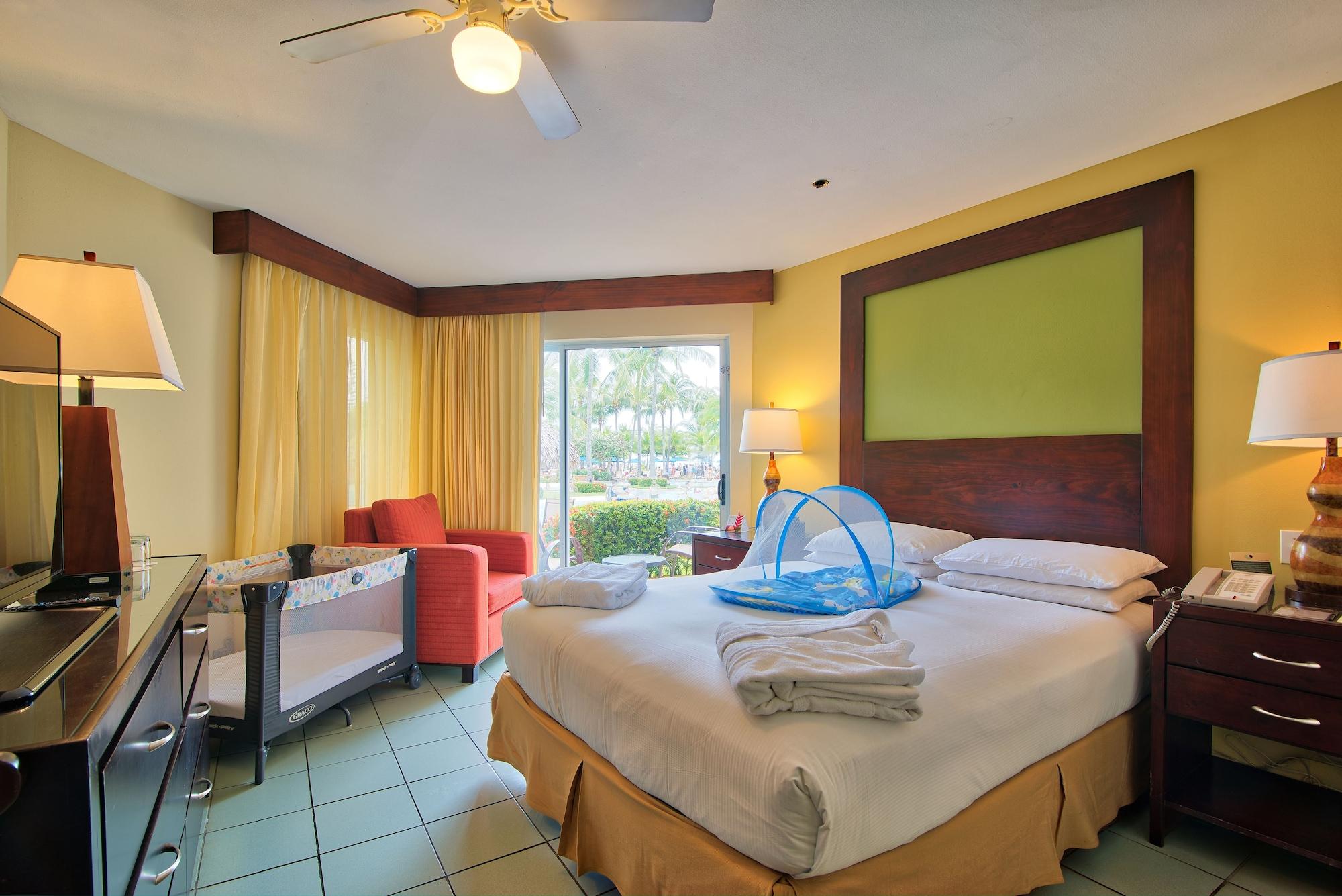Fiesta Resort All Inclusive Central Pacific - Costa Rica El Roble Exterior photo The photo shows a cozy hotel room with a bright and cheerful atmosphere. It features a light green accent wall and has a large window with sheer curtains allowing natural light to enter. There is a comfortable king-sized bed with crisp white linens a