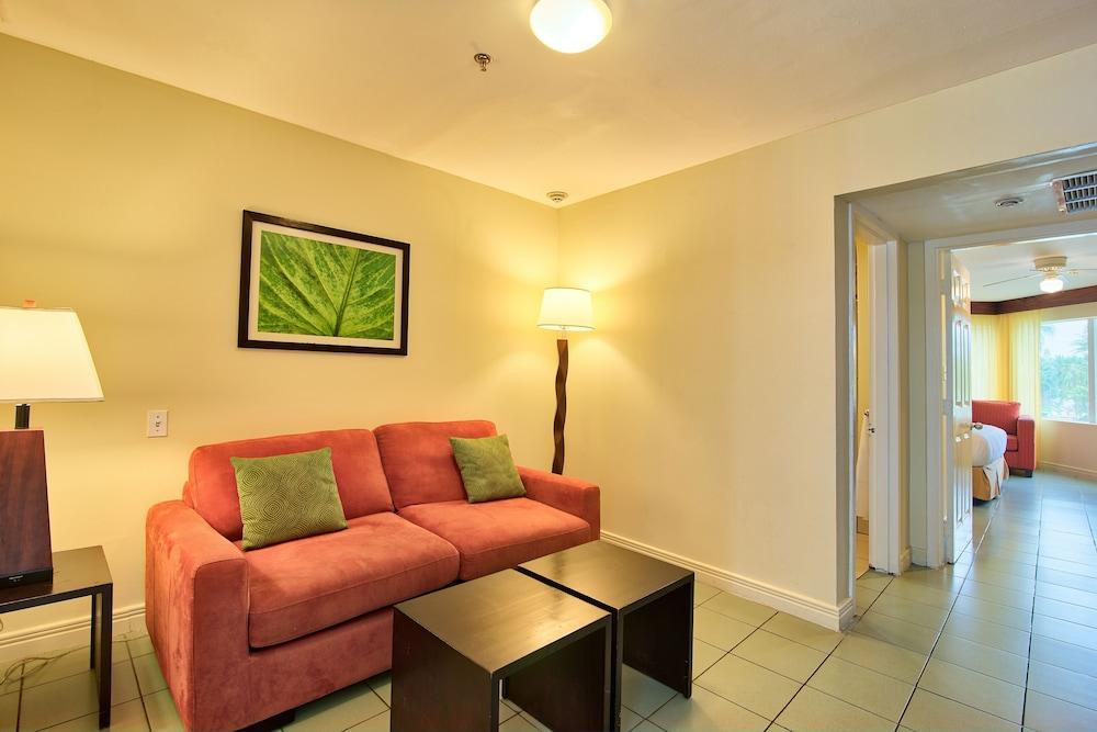 Fiesta Resort All Inclusive Central Pacific - Costa Rica El Roble Exterior photo The photo shows a cozy living area featuring a bright and inviting atmosphere. It includes a red sofa with two green cushions, accompanied by two small black coffee tables in front. The wall has a framed artwork depicting a green leaf. There is also 