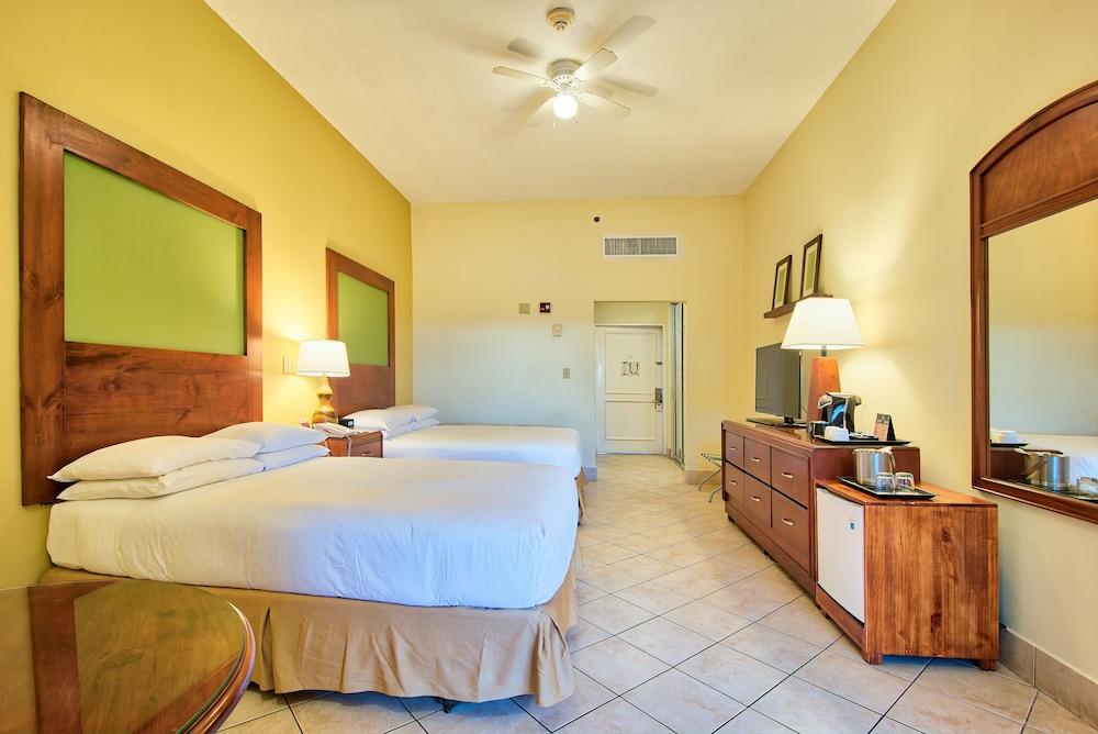 Fiesta Resort All Inclusive Central Pacific - Costa Rica El Roble Exterior photo The photo shows a hotel room with a bright and inviting atmosphere. It features two beds with white linens and wooden headboards, situated across from each other. There are bedside lamps on each side of the beds, providing soft lighting. 

The walls 