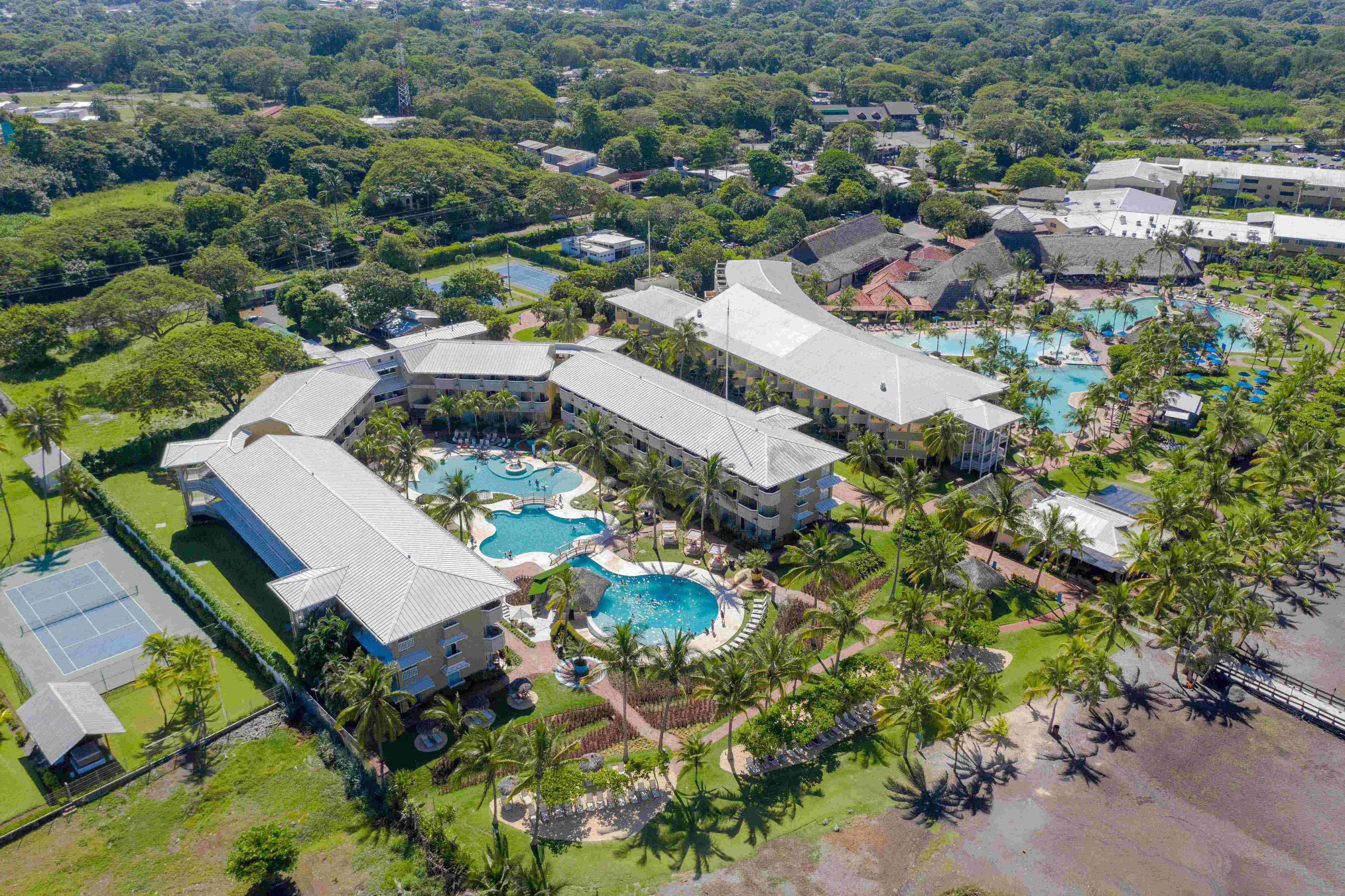 Fiesta Resort All Inclusive Central Pacific - Costa Rica El Roble Exterior photo The photo shows an aerial view of a resort or hotel complex surrounded by lush greenery. The buildings feature a light color and have multiple sections with distinct rooftops. In the foreground, there are several swimming pools with different shapes,