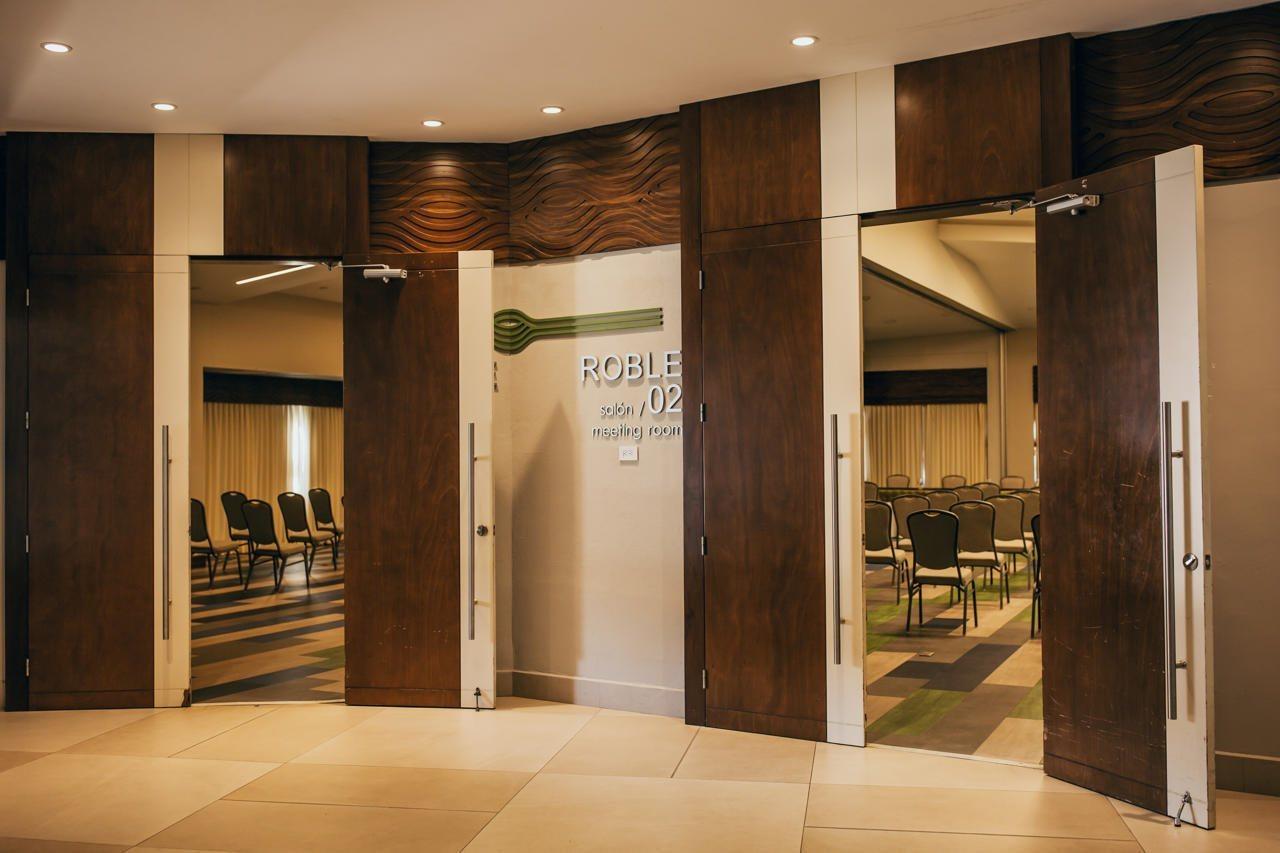 Fiesta Resort All Inclusive Central Pacific - Costa Rica El Roble Exterior photo The photo depicts a hallway leading to a meeting room identified as "Roble, Room #102." The entrance features double doors made of wood and glass, with signage indicating the room number. Behind the doors, there are rows of chairs arranged in a forma