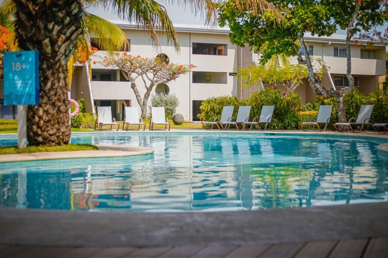 Fiesta Resort All Inclusive Central Pacific - Costa Rica El Roble Exterior photo The photo shows a serene swimming pool surrounded by greenery and lounge chairs. In the background, there are white buildings with balconies. Palm trees and other plants add to the tropical ambiance, making it a relaxing and inviting space. The water