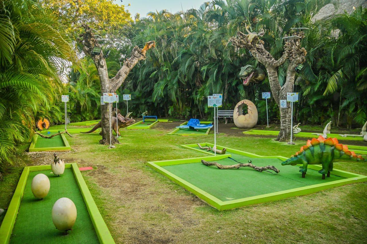 Fiesta Resort All Inclusive Central Pacific - Costa Rica El Roble Exterior photo The photo displays a mini-golf course set in a lush, tropical environment. The course features vibrant green putting areas surrounded by decorative elements like dinosaur sculptures, large eggs, and themed obstacles. There are trees with unique shape