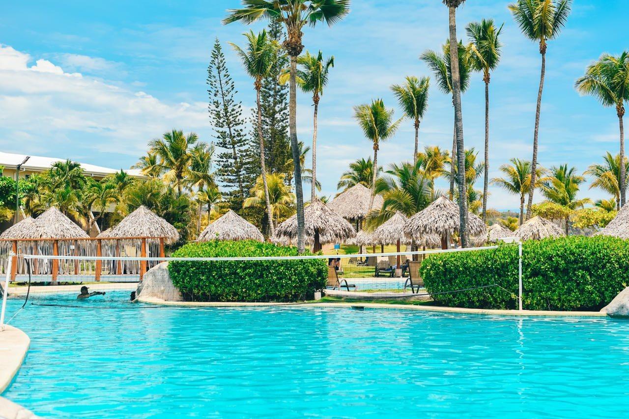 Fiesta Resort All Inclusive Central Pacific - Costa Rica El Roble Exterior photo The photo shows a beautiful outdoor swimming pool set in a tropical environment. The water is a clear turquoise color. Surrounding the pool are lush green bushes and palm trees, providing a relaxing atmosphere. In the background, there are several th