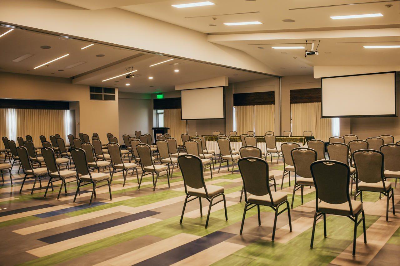 Fiesta Resort All Inclusive Central Pacific - Costa Rica El Roble Exterior photo The photo shows a spacious room set up for an event or meeting. There are several rows of chairs arranged facing two screens, which are likely used for presentations. The flooring features a combination of green and blue patterns, and the overall lig