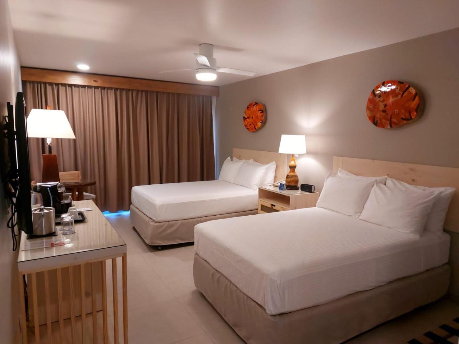 Fiesta Resort All Inclusive Central Pacific - Costa Rica El Roble Exterior photo The photo shows a hotel room with two queen-sized beds, each made up with white linens and pillows. There are bedside tables with lamps beside each bed. A flat-screen television is mounted on the wall across from the beds. To the left, there’s a wood