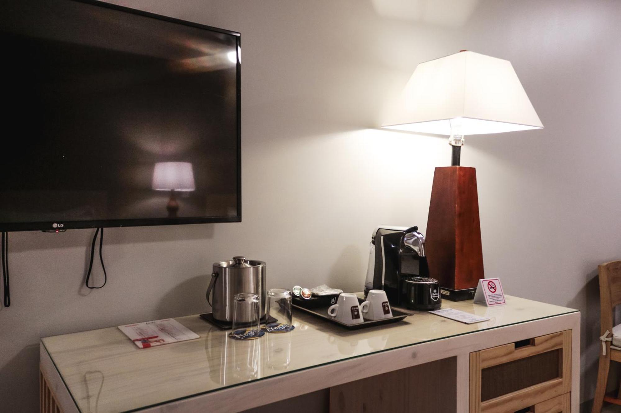Fiesta Resort All Inclusive Central Pacific - Costa Rica El Roble Exterior photo The photo shows a corner of a room featuring a TV mounted on the wall. Below the TV, there is a wooden console or table. On the table, there is a coffee maker, cups, and a kettle. A lamp with a lampshade is also on the table, providing ambient lighti